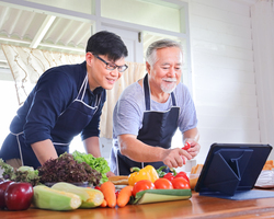 A father and son looking at a recipe on a computer and peeling vegetables.